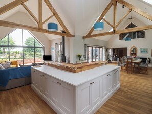 A spacious living area with a large wooden beam ceiling, a central island with a white countertop, and a dining area with a wooden table and chairs. - Crossett Grange (Driffield)