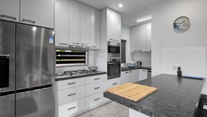 A modern kitchen with stainless steel appliances, white cabinetry, and a wooden cutting board.