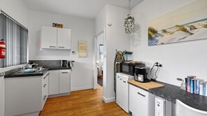 A modern kitchen with white cabinets, a black countertop, and a wooden floor. There is a fire extinguisher on the wall, a painting of a beach scene, and a few books on the counter. - Secret on Seagrass by Book Jervis Bay (Vincentia)