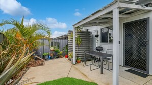 A covered patio with a table and chairs, surrounded by potted plants and a water tank. - Secret on Seagrass by Book Jervis Bay (Vincentia)