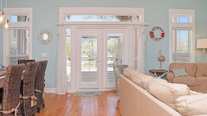 A living room with wicker chairs, a beige sofa, and a view through a glass door.