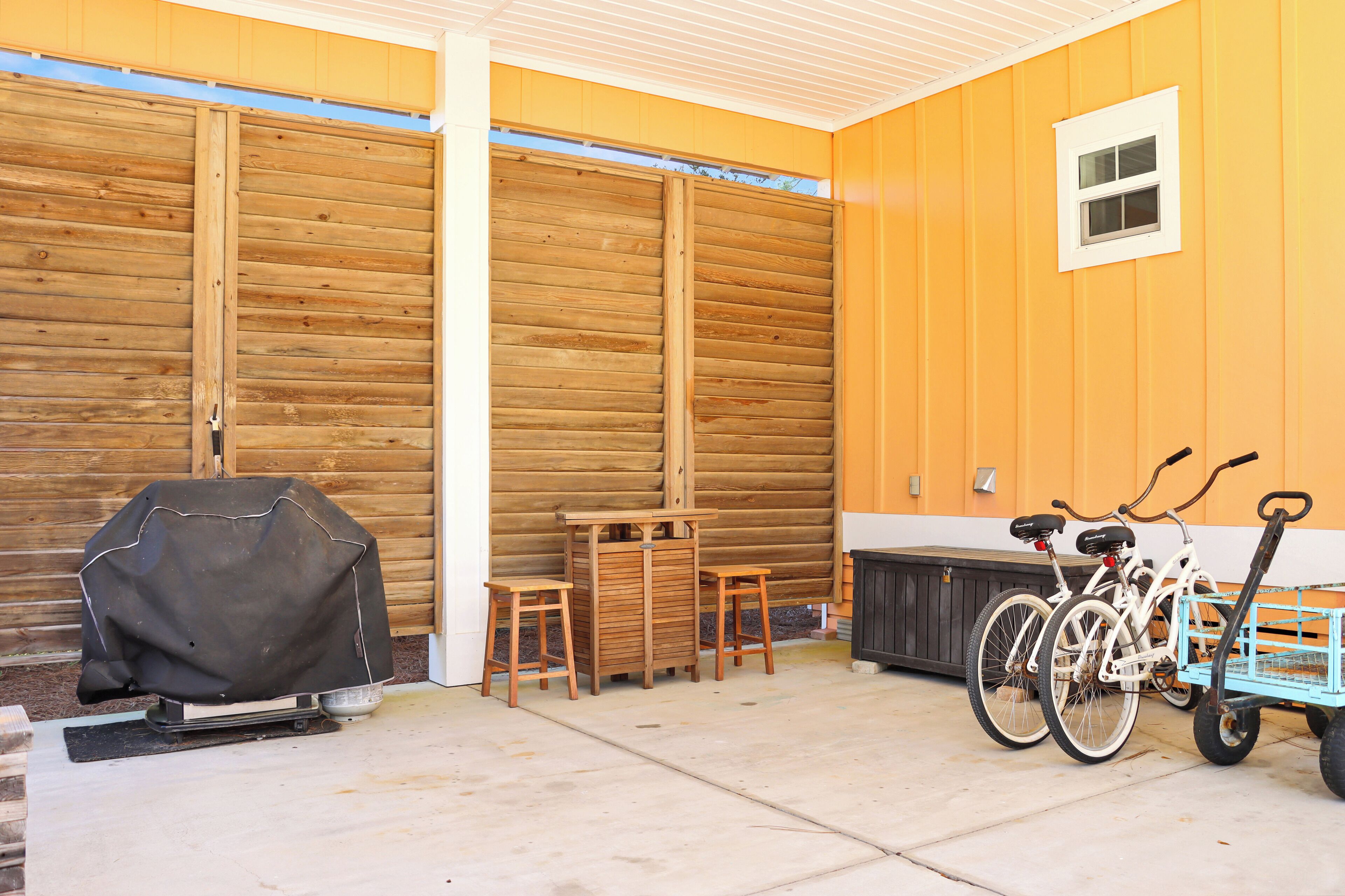 A covered patio area with a barbecue grill, wooden table and chairs, and bicycles.