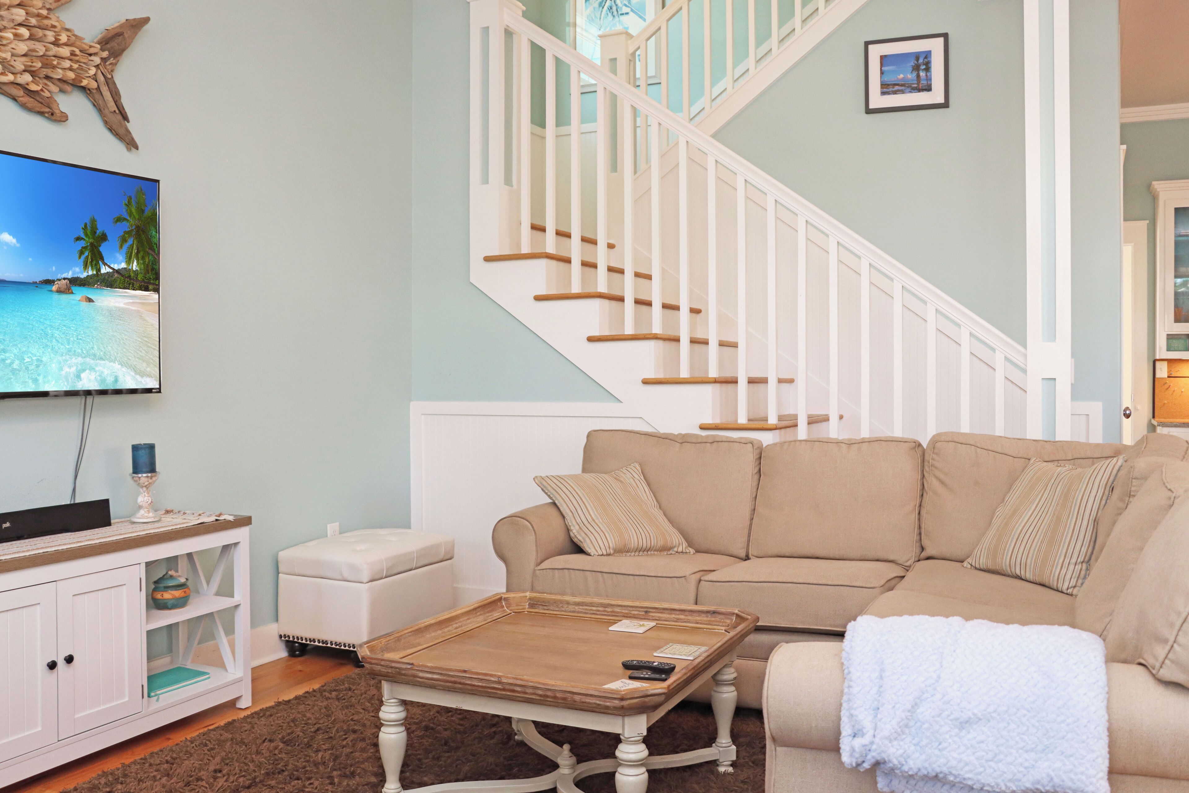A living room with a beige sofa, a coffee table, a TV, and a staircase.