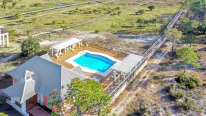 A house with a swimming pool, surrounded by a wooden deck and a view of the beach.