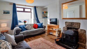 Ein gemütliches Wohnzimmer mit einer Couch, einem Fernseher, einem Kamin und Meerblick durch ein Fenster.