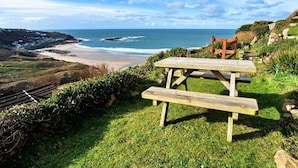 Ein Picknicktisch auf einer grasbewachsenen Anhöhe mit Blick auf einen Strand, an dem Wellen brechen.
