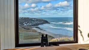 A window with a view of a coastal landscape, including a beach and rocky terrain. - Bishop Rock (Sennen)