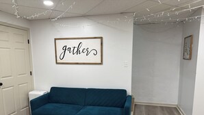 Ein Zimmer mit einem türkisfarbenen Sofa, einer weißen Tür und einem an der Wand befestigten Schild mit der Aufschrift 'gathers'.