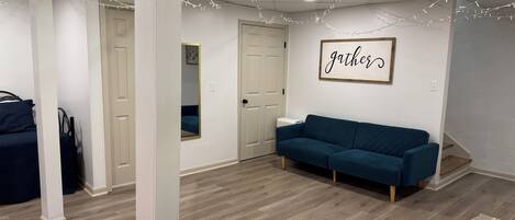 A modern, well-lit room with a blue sofa, a mirror, and a 'gather' sign on the wall.