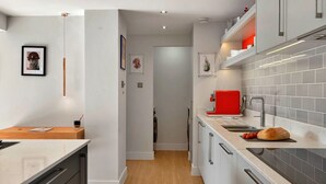 A modern kitchen with white cabinets, a red appliance, and a wooden floor.