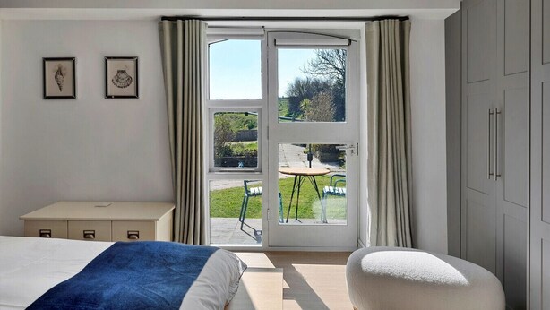 A bedroom with a bed, a desk, and a view of the outdoors through a sliding glass door.