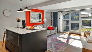 A modern kitchen with a central island, a dining area with a sofa and a rug, and a large sliding glass door leading to a garden.