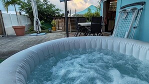An inflatable hot tub in a backyard with a table and chairs, a potted plant, and a blue building in the background. - L'Althéa Bleu, 2 minutes from the sargasso-free beach  (Sainte-Rose)