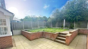 A patio area with tiled flooring, brick planters, and a wooden fence. - Spacious Central Home - Sleeps 7, Garden & Parking (Sheffield)