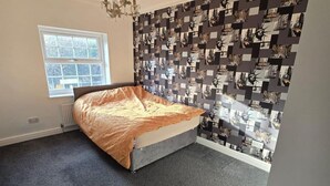 A bedroom with a bed, a window, and a wall covered with a patterned wallpaper. - Spacious Central Home - Sleeps 7, Garden & Parking (Sheffield)