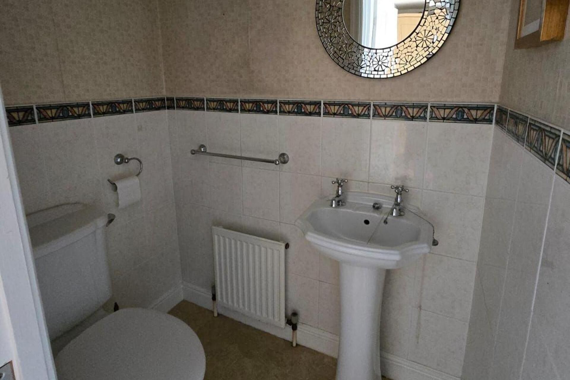 A bathroom with a toilet, a sink, a radiator, and a mirror.