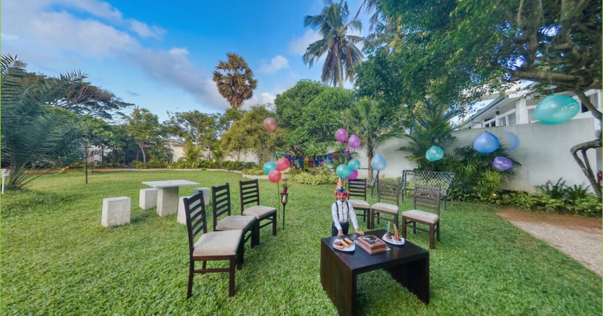 Un jardín al aire libre con una mesa y sillas, rodeado de follaje y globos.