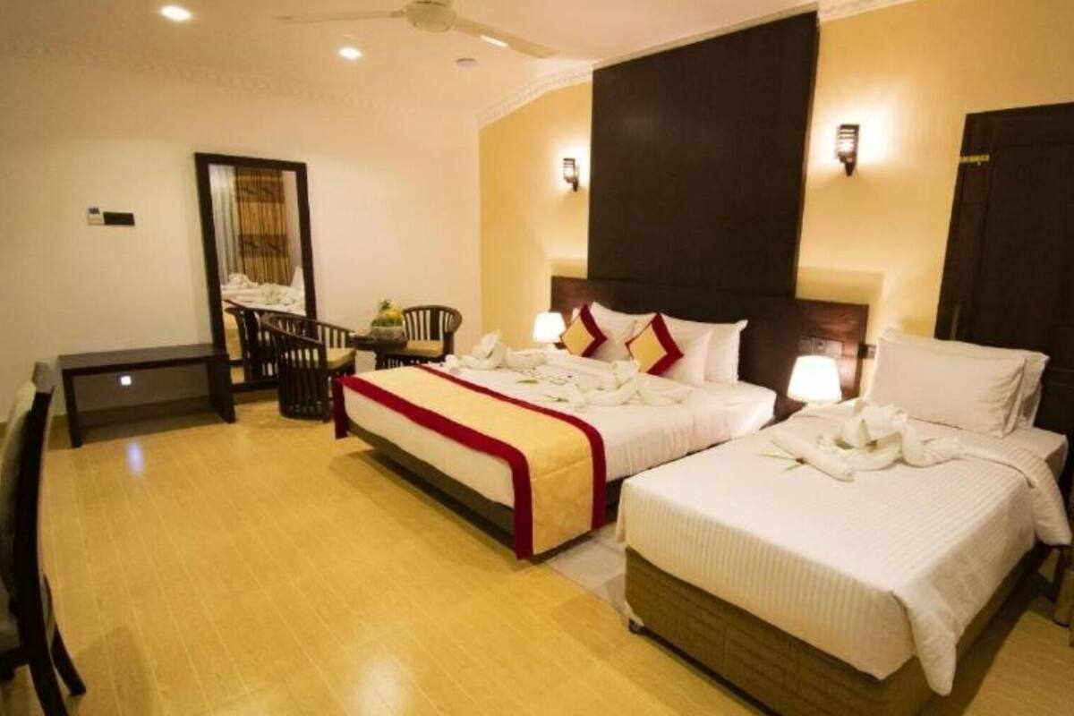 A hotel room with two beds, a desk, and a mirror.