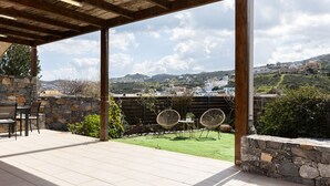 A covered patio with stone walls, a table, chairs, and a view of a hillside town. - Villa Misemeli (Agia Pelagia)
