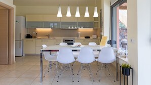 A modern kitchen with white cabinets, a dining table with four chairs, and pendant lights. - Villa Misemeli (Agia Pelagia)