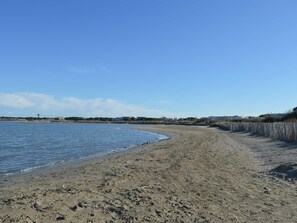 A sandy beach with a clear sky, a wooden fence, and buildings in the background.