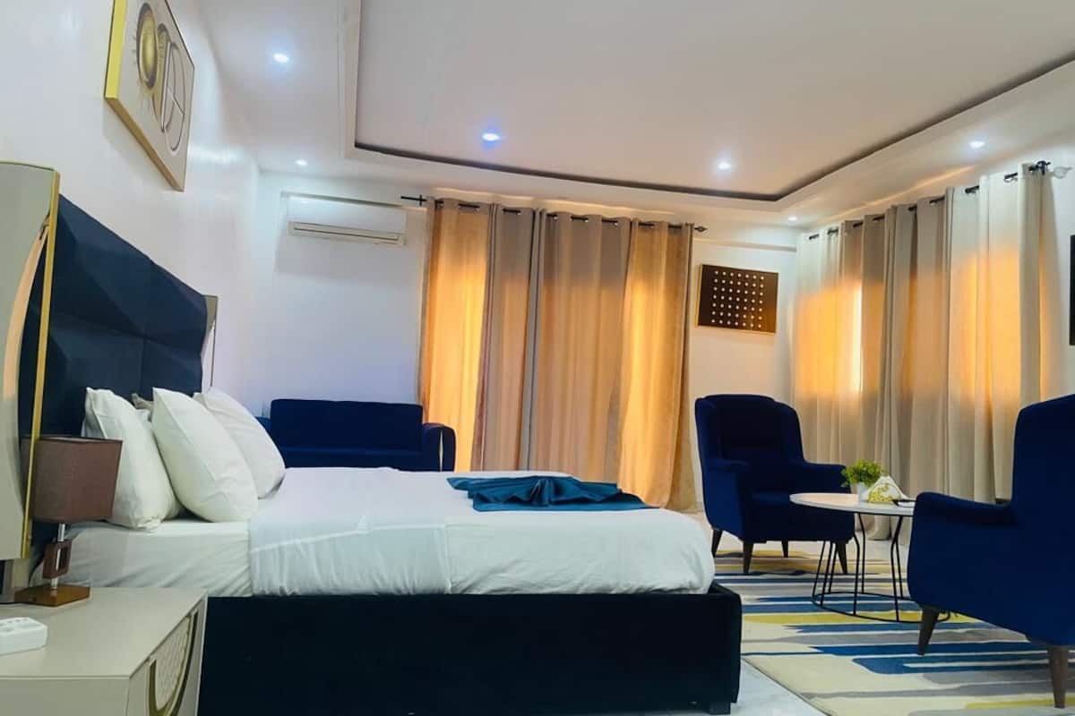 Una habitación de hotel moderna con una cama grande, un escritorio con lámpara, una silla y una pequeña mesa con una planta.