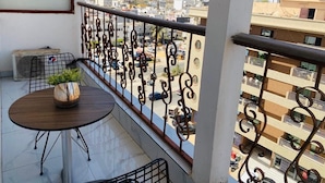 Een balkon met een ronde tafel en stoelen, een bloempot en uitzicht op de stad.