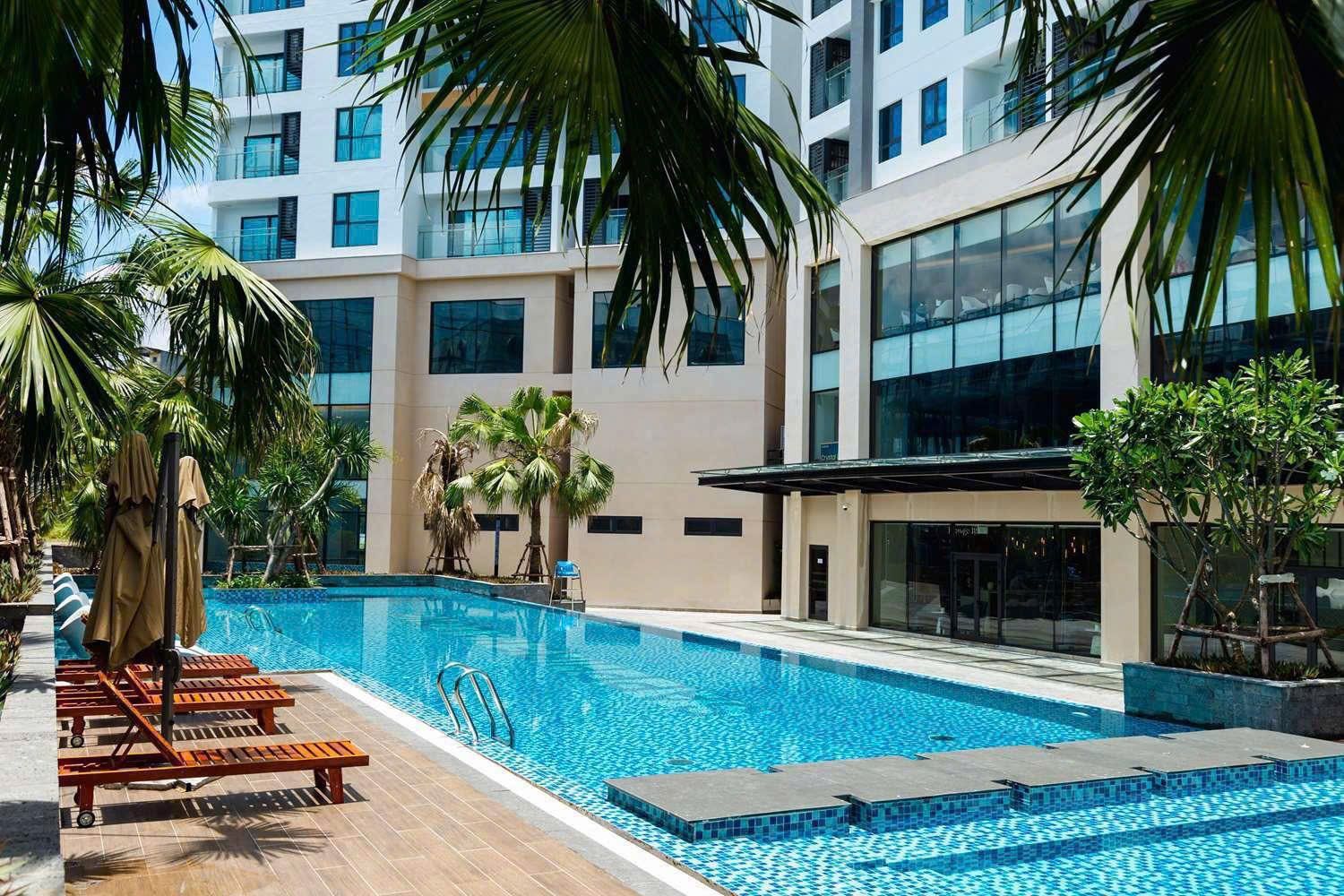 A swimming pool with lounge chairs and palm trees, surrounded by a modern building with large windows.