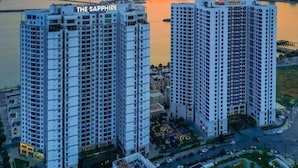 Un edificio de gran altura llamado "THE SAPPHIRE" con vistas a un atardecer sobre una masa de agua y un paisaje urbano de fondo.