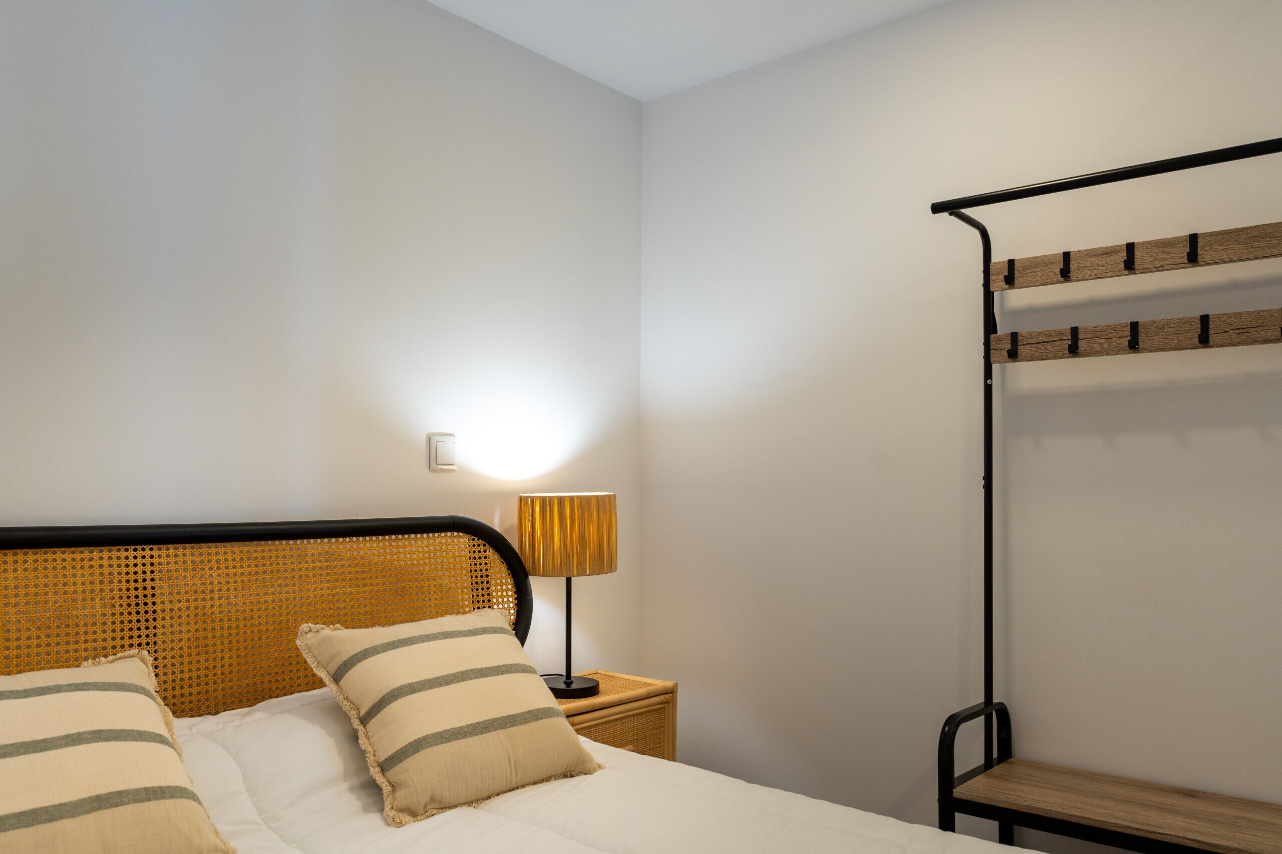 A bed with a woven headboard, two pillows, a bedside lamp, and a wooden bench against the wall.