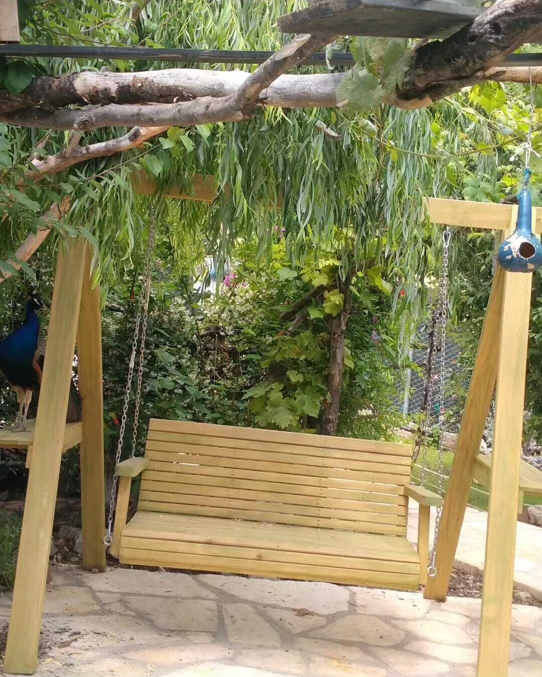 Une balançoire en bois avec un banc, entourée de verdure et de plantes grimpantes.