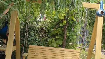 Une balançoire en bois avec un banc, entourée de verdure et de plantes grimpantes.