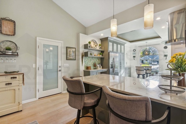 A modern kitchen with a large island, pendant lights, and a view to the dining area.