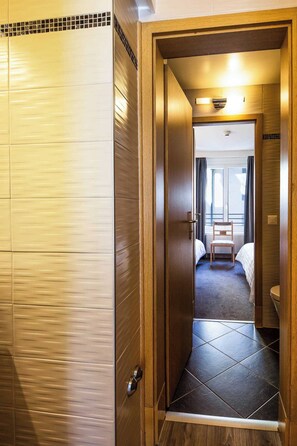 Una habitación de hotel con puerta de madera, una mesita pequeña, dos camas y una ventana con cortinas.