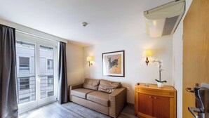 A hotel room with a sofa, a wooden cabinet, a wall-mounted lamp, and a framed artwork. - Charming Apartment - 1br-4p- Geneva (Geneva)