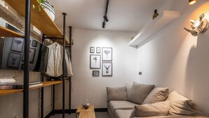A modern living room with a sofa, a coffee table, and a shelf with clothes and framed pictures. - O&O Group - Kolonaki Urban Residence (Athens)