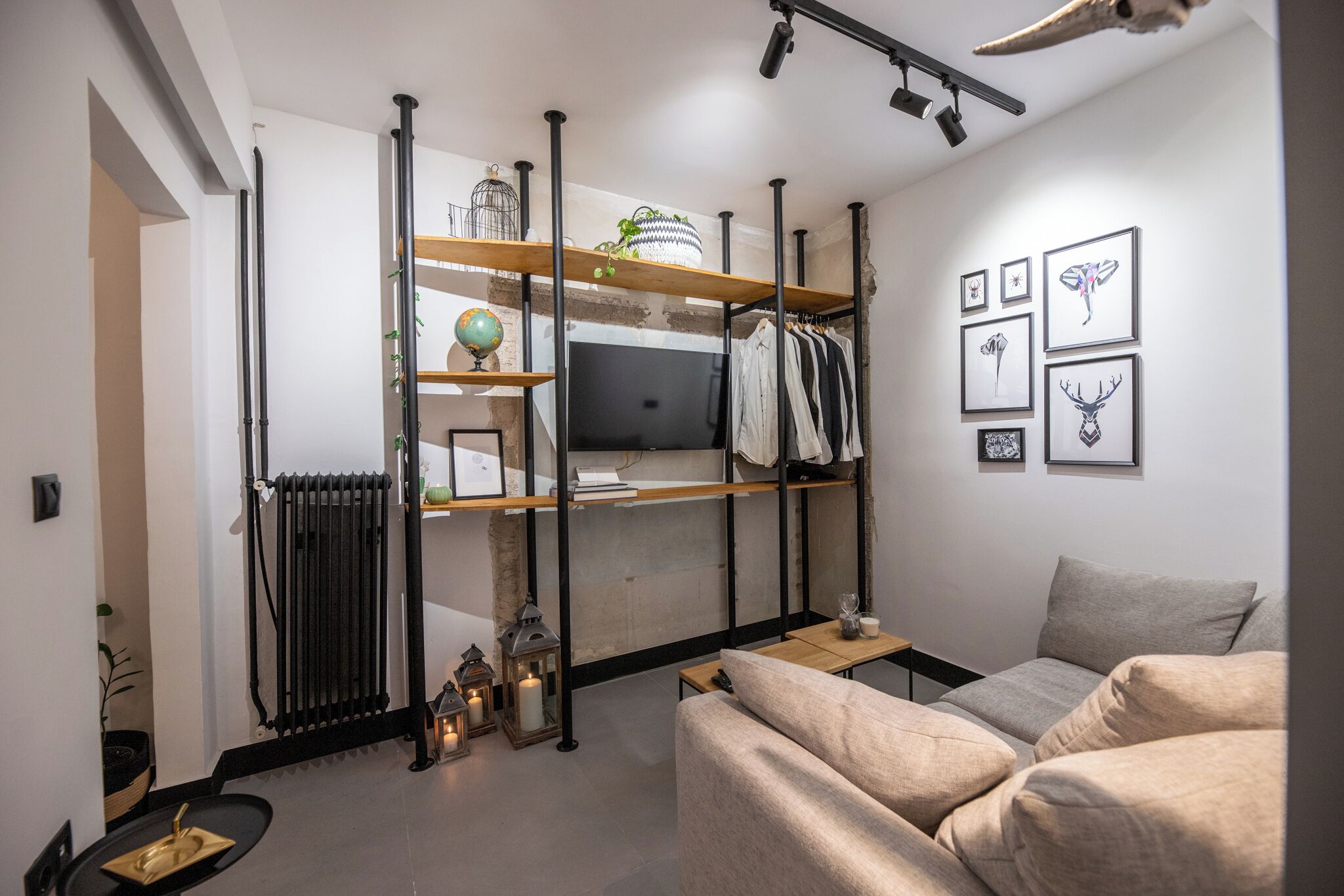En moderne stue med sofa, fjernsyn, reoler med pyngegenstande og en radiator.