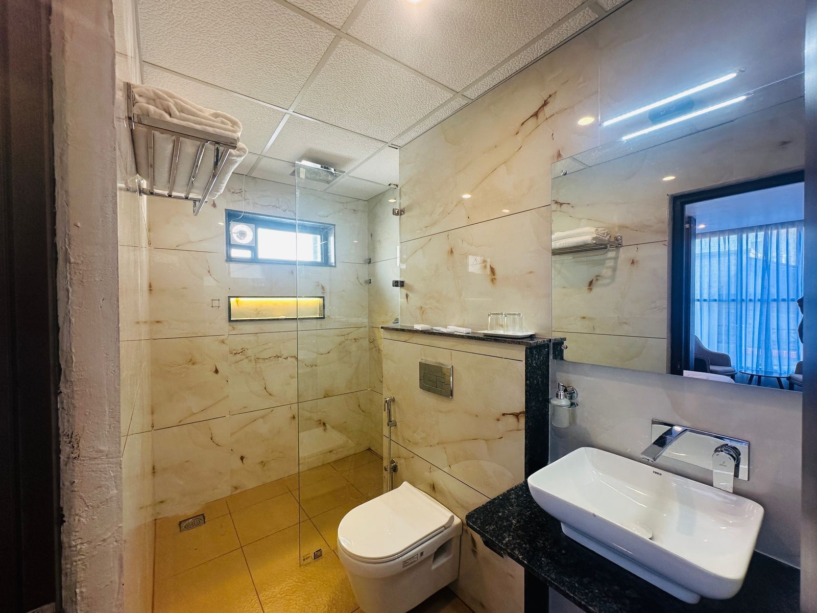 Un baño moderno con ducha de vidrio, inodoro blanco, lavamanos con espejo y un perchero para toallas.