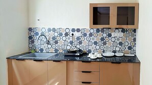 Ett kompakt kök med en svart bänkskiva, en diskho och ett hexagonalt mönstrat stänkskydd. Det finns två skåp med en trädörr och ett litet fönster ovanför diskhon.