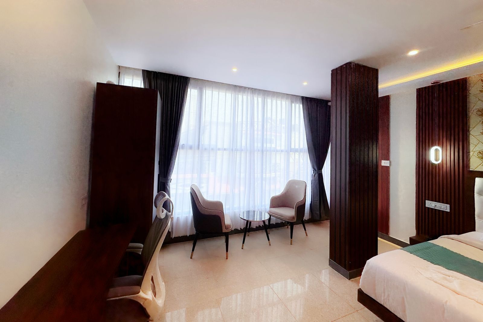 A hotel room with a bed, two chairs, a small table, and a large window with curtains.