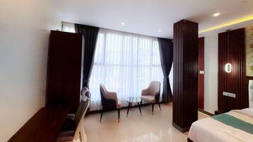 A hotel room with a bed, two chairs, a small table, and a large window with curtains.
