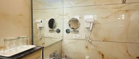 A bathroom with a white sink, two mirrors, a vanity with a marble countertop, and a handheld showerhead.