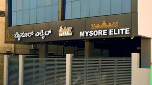En byggnad med en skylt som visar orden "Maximus" och "MYSORE ELITE", och en logotyp som föreställer en tempelliknande struktur.