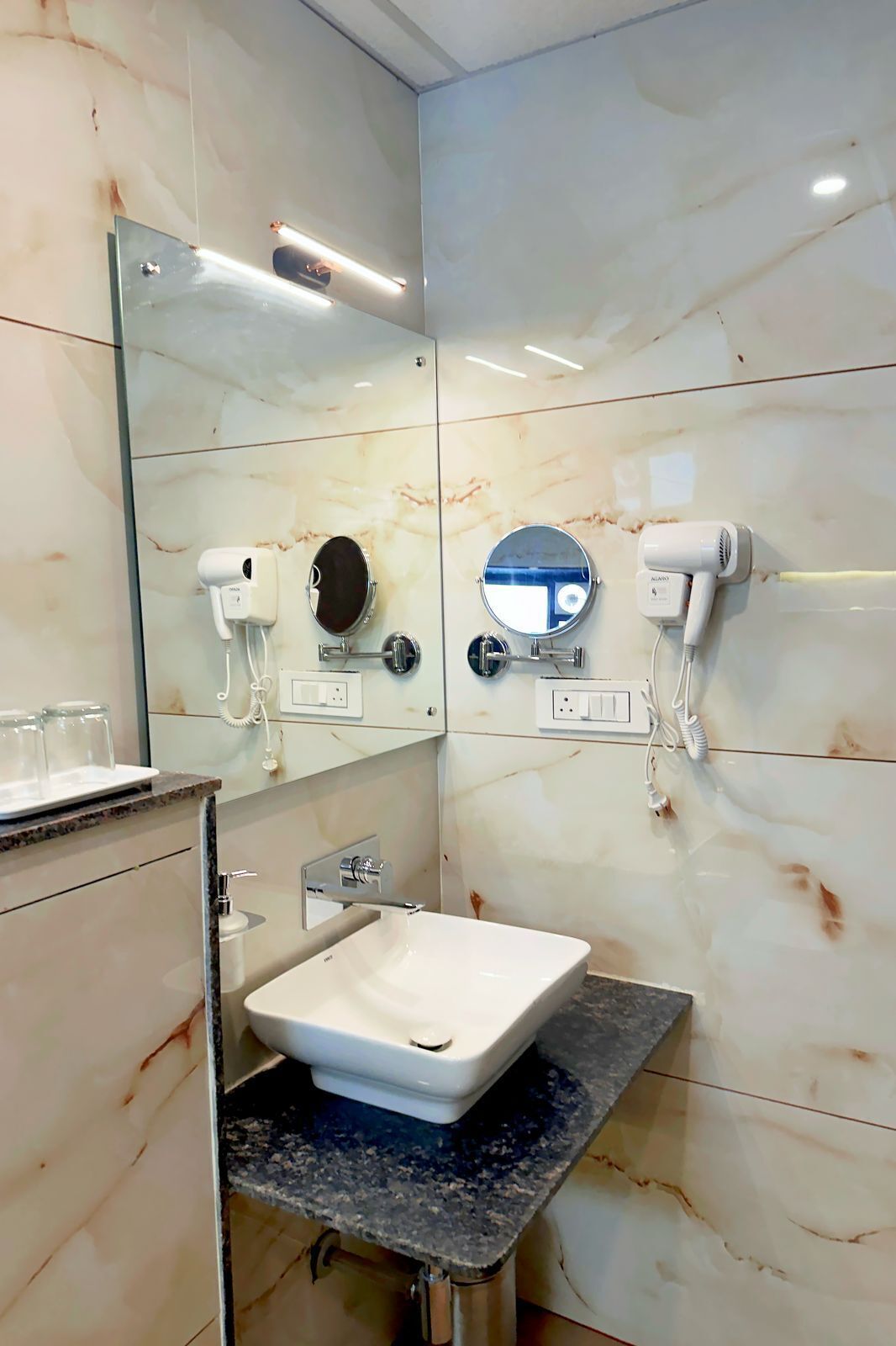 Une salle de bain moderne avec un lavabo blanc, deux miroirs, un sèche-cheveux et une douchette à main.