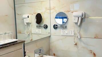 A modern bathroom with a white sink, two mirrors, a hairdryer, and a handheld showerhead.