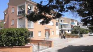 A multi-story residential building with balconies, a gated entrance, and a clear sky.