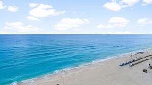 A beach with clear blue water, a sandy shore, and a row of blue umbrellas. - Treasure Island condo - pool, hot tub and gulf views (Panama City Beach)
