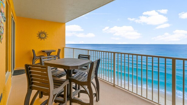 A balcony with a table and chairs, overlooking a beach with clear blue water and a sunny sky. - Treasure Island condo - pool, hot tub and gulf views (Panama City Beach)
