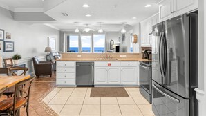 A modern kitchen with white cabinets, stainless steel appliances, and a view of the ocean. - Treasure Island condo - pool, hot tub and gulf views (Panama City Beach)