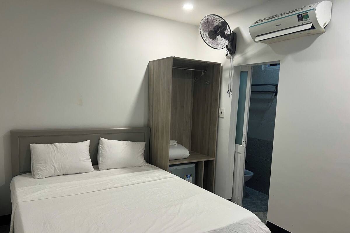 Une chambre d’hôtel équipée d’un lit, d’une armoire en bois, d’un ventilateur sur pied et d’un appareil de climatisation.